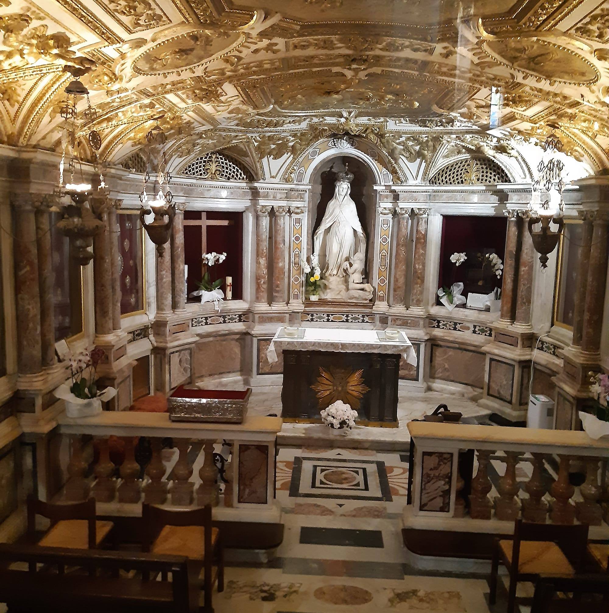 Interno di una cripta con affreschi dorati, colonne marmoree e statua della Vergine.