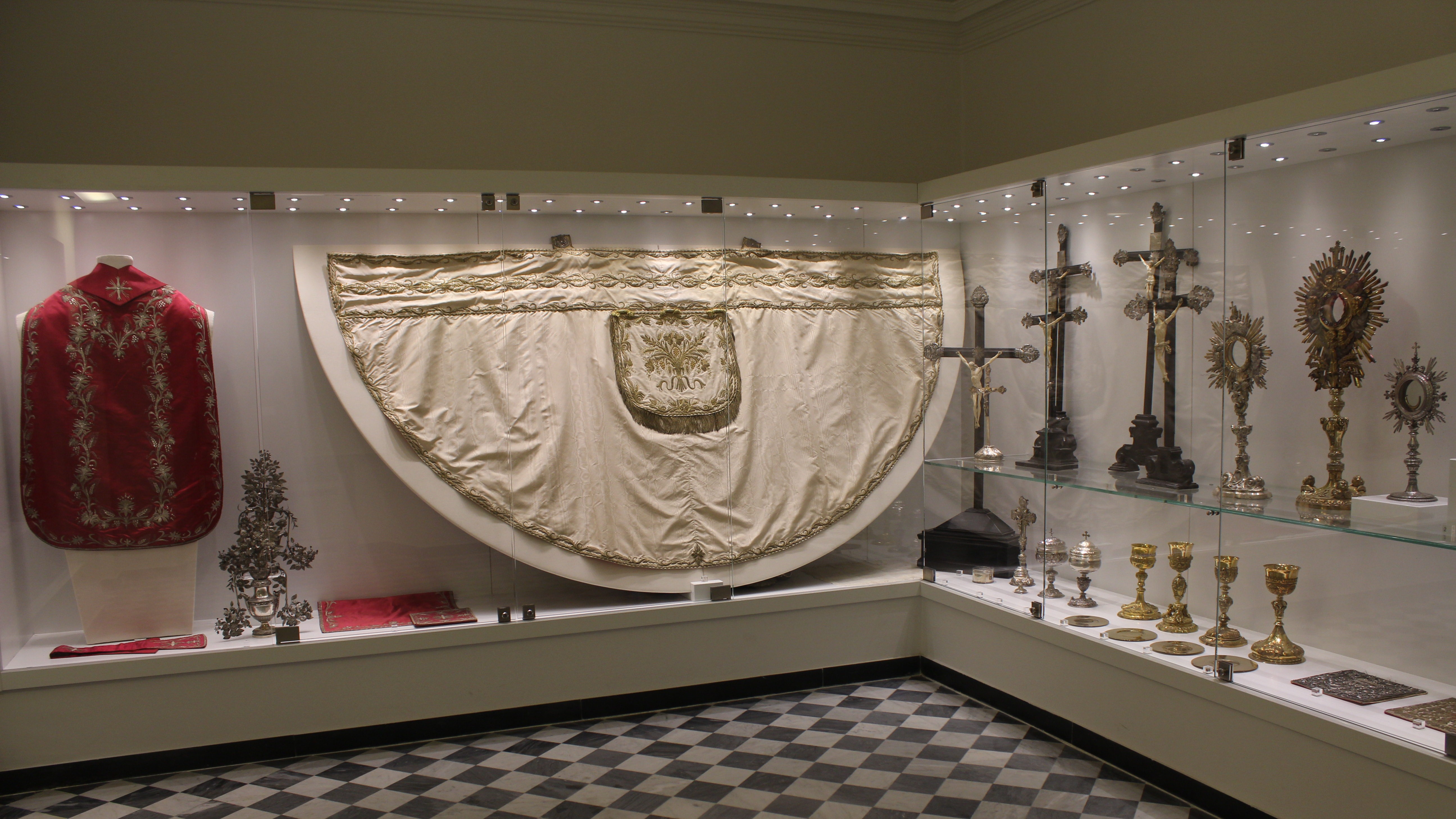 Vetrina museale presso il museo del Santuario di Savona, con antichi paramenti sacri, croci e calici liturgici.