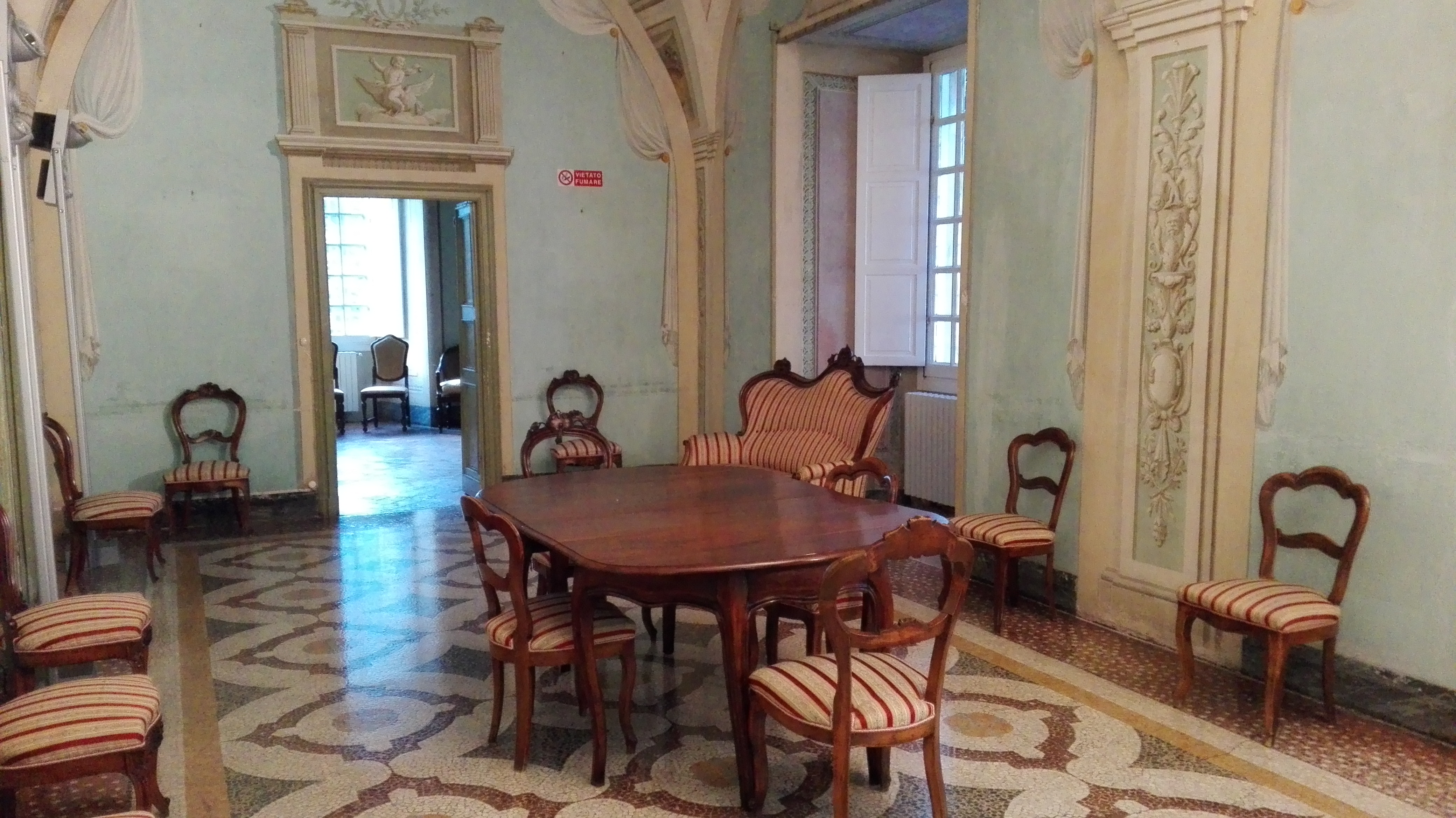 Sala storica del Santuario di Savona con arredi d’epoca, stucchi decorati e tavolo in legno circondato da sedie imbottite.