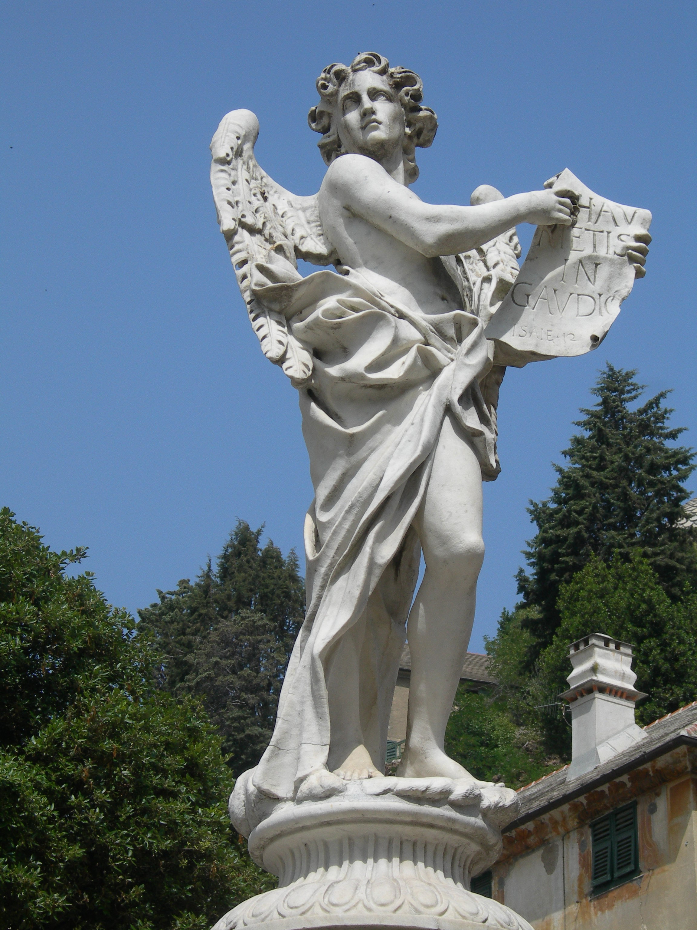 Scultura di un angelo in marmo bianco con un cartiglio, parte di una fontana monumentale.