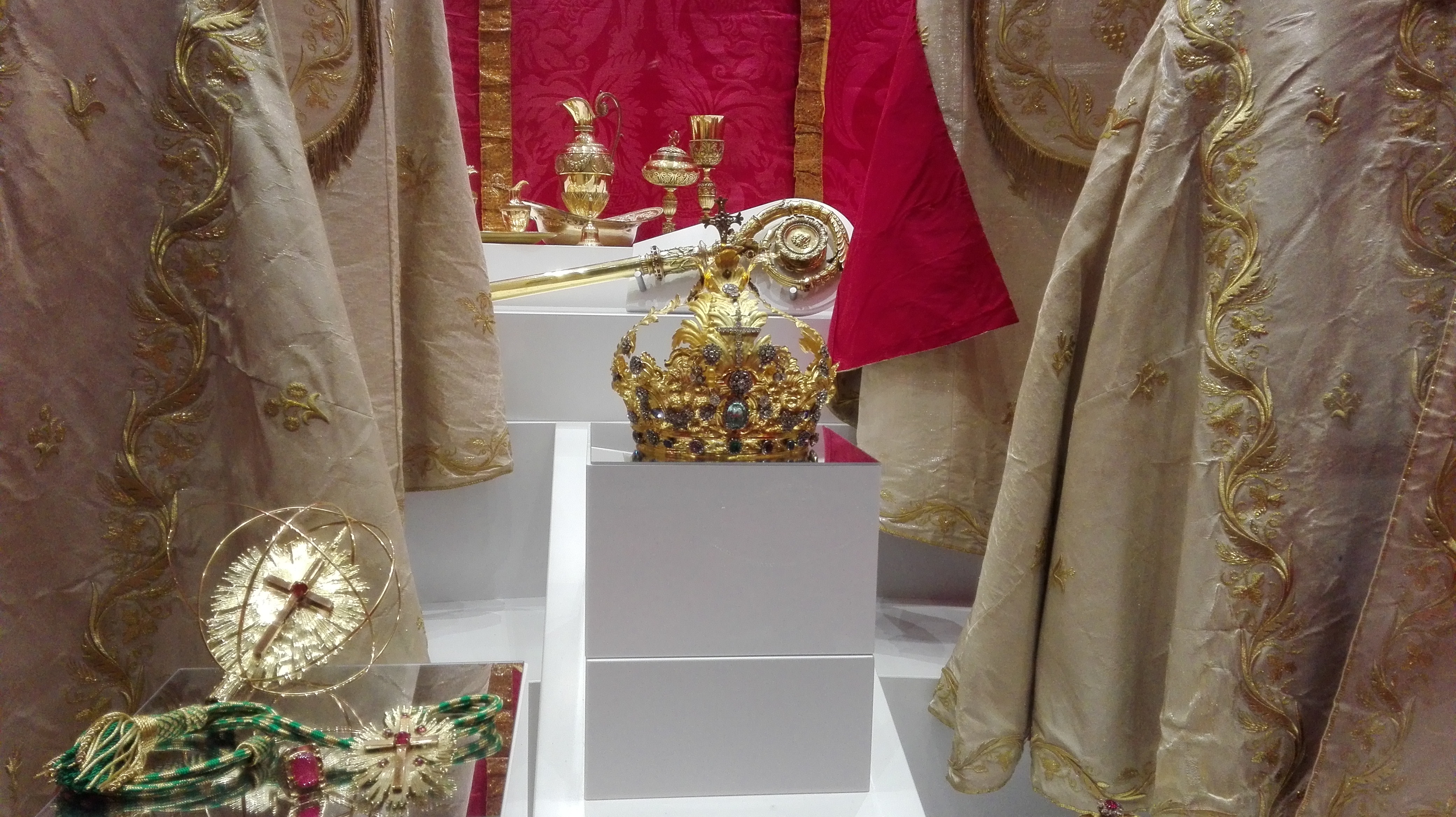 Vetrina espositiva con paramenti sacri ricamati in oro, corone e oggetti liturgici.