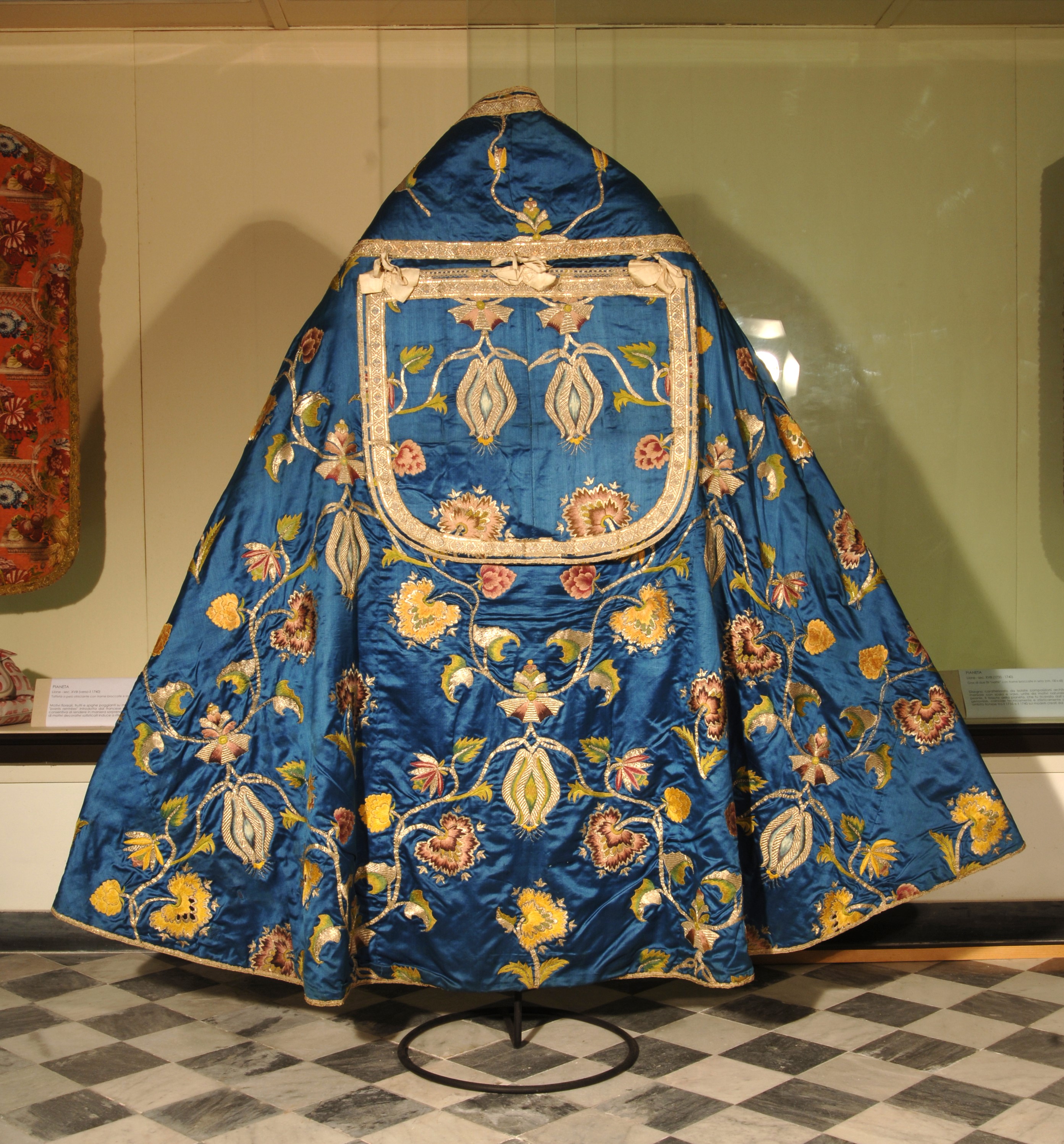 Paramento sacro in seta blu con ricami dorati di fiori e motivi ornamentali.